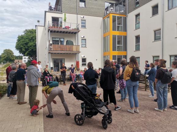 Eine Menschengruppe steht im Kreis vor dem Wohnprojekt Querbeet