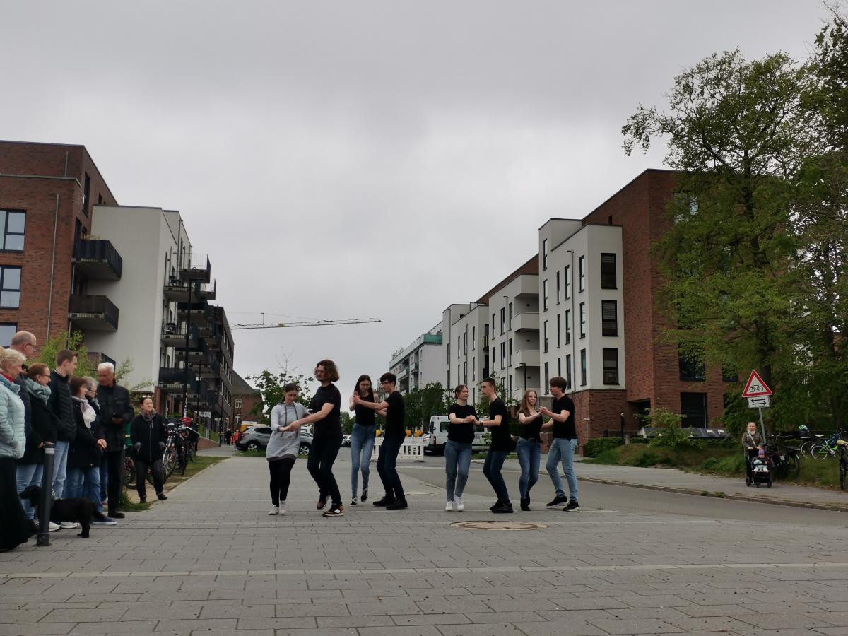 Junge Erwachsene tanzen in Zweierpaaren vor einer Häuserflucht